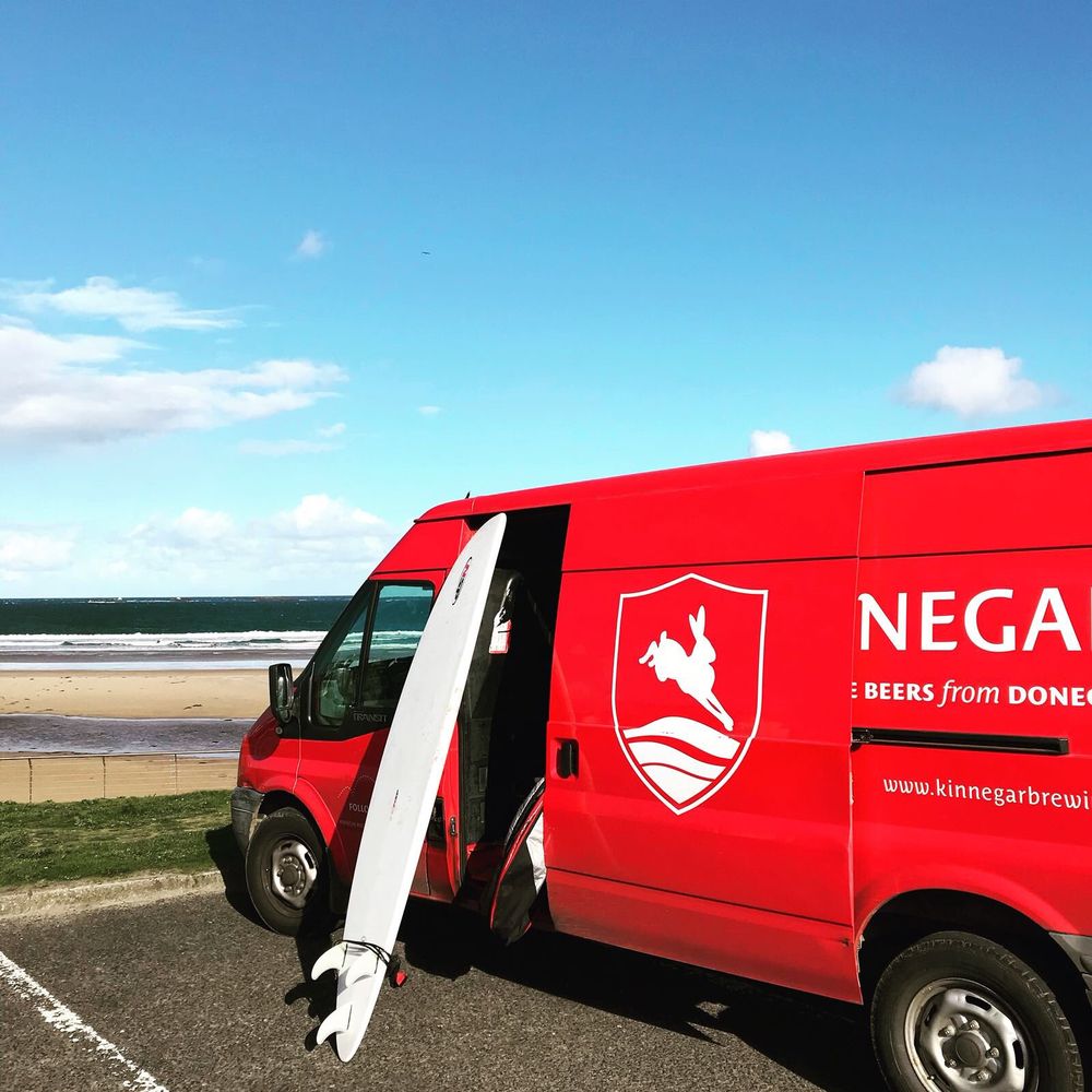 Il furgone rosso di Kinnegar con una tavola da surf, davanti a una spiaggia del Donegal