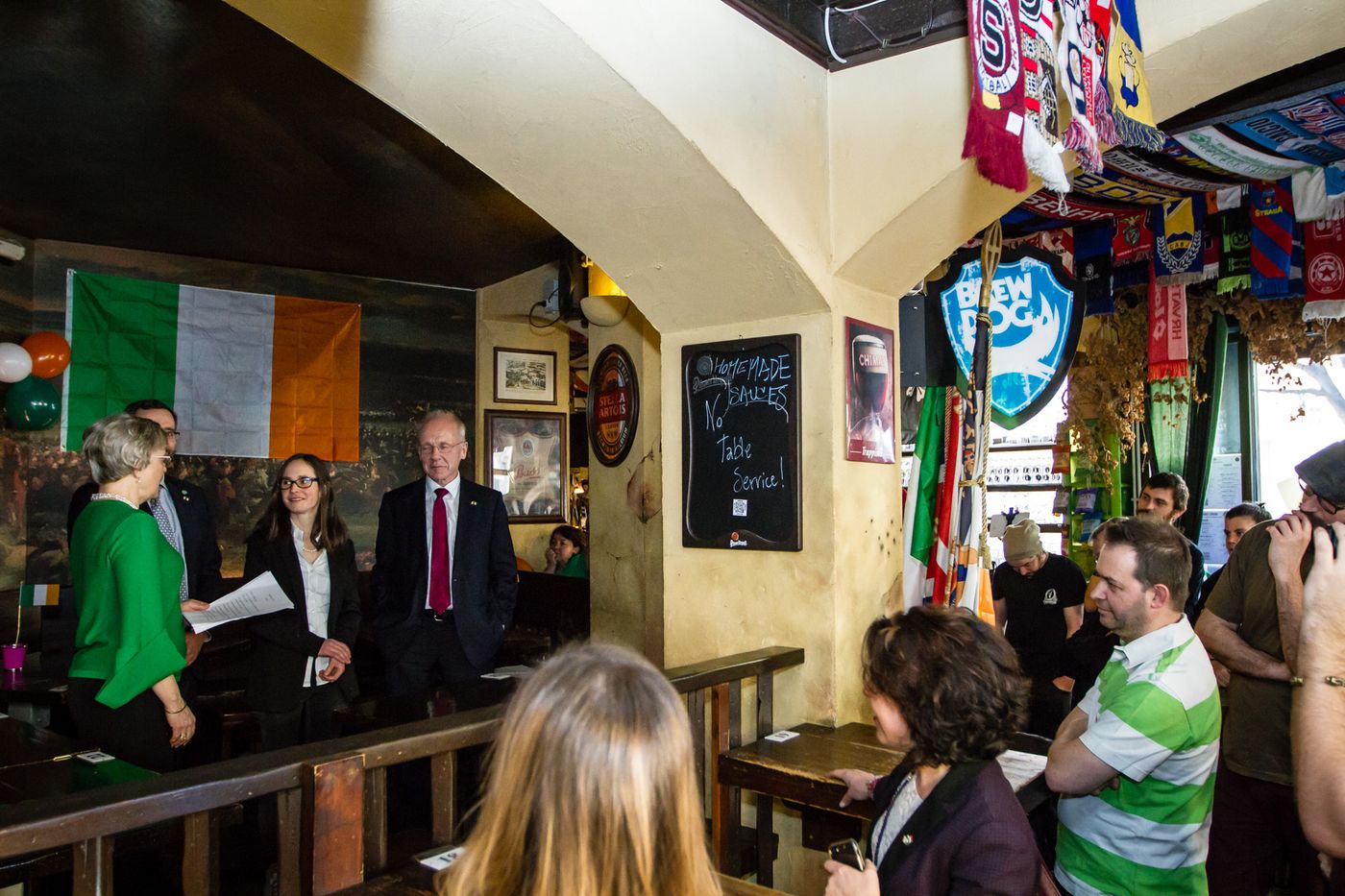 La sala de La Belle Alliance durante l'apertura: i publican in ascolto, sullo sfondo gli ospiti irlandesi e la bandiera